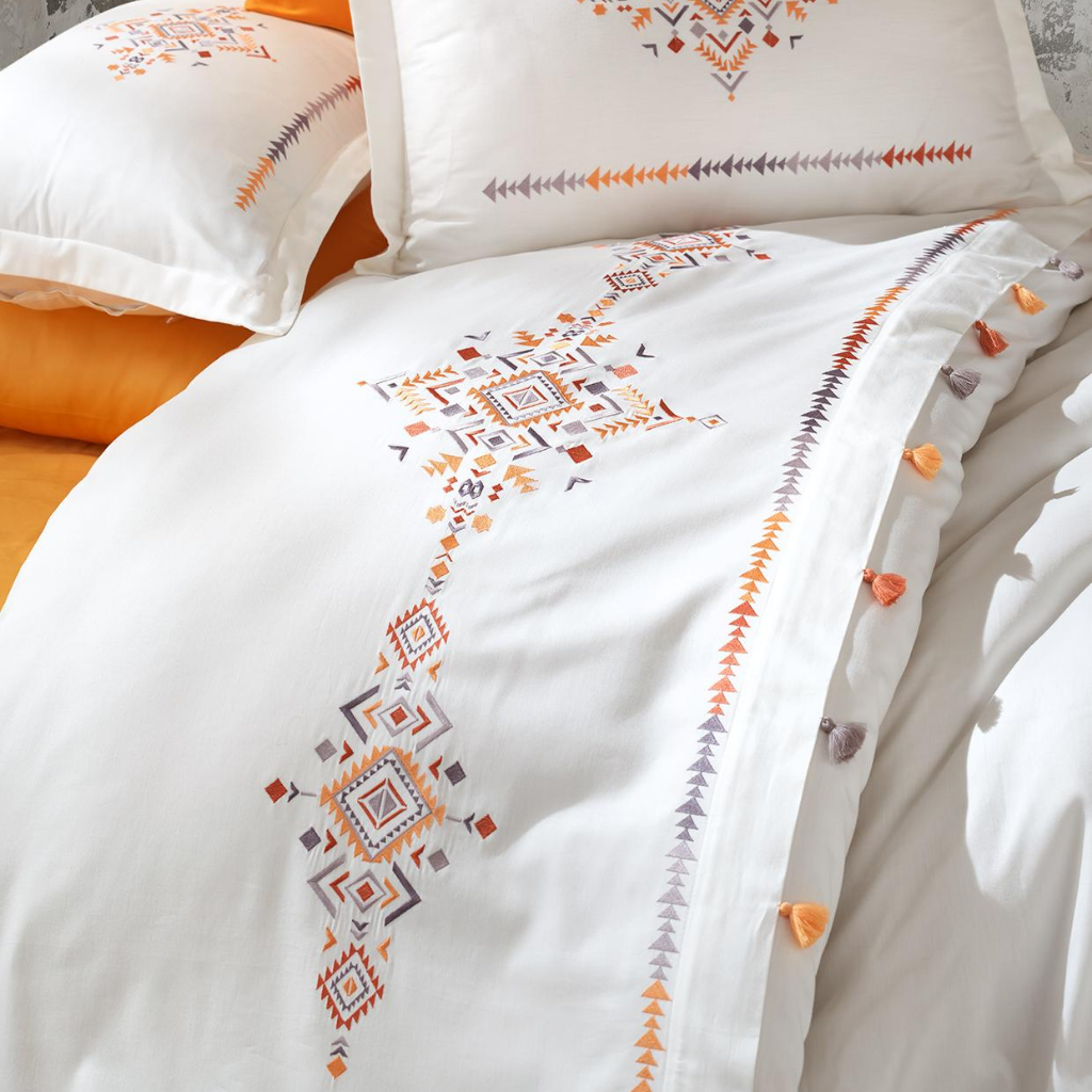 Orange, yellow and grey embroideries and tassels pairs with orange, cotton-sateen bed sheet.