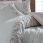 White duvet cover is adorned with pink, green and blue floral embrioderies and pairs with pink bed sheet and pillowcases
